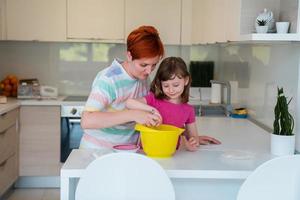 divertente poco ragazza aiutante giocando con Impasto su il suo mani apprendimento per impastare aiuta adulto mamma nel il cucina, contento carino bambino figlia e genitore mamma avere divertimento cucinando biscotti. foto