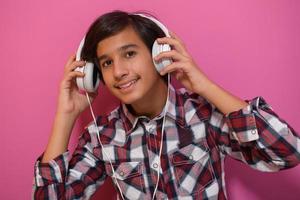 Arabo adolescenziale ragazzo indossare cuffie e ascoltando per musica rosa sfondo foto