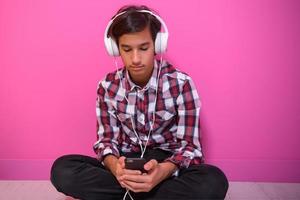 Arabo adolescenziale ragazzo indossare cuffie e ascoltando per musica rosa sfondo foto