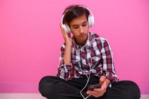 Arabo adolescenziale ragazzo indossare cuffie e ascoltando per musica rosa sfondo foto