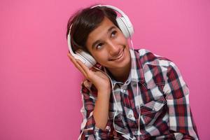 Arabo adolescenziale ragazzo indossare cuffie e ascoltando per musica rosa sfondo foto