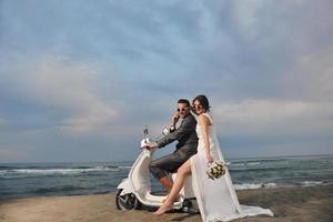 appena sposato coppia su il spiaggia cavalcata bianca scooter foto