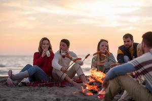 gruppo di giovane amici seduta di il fuoco a spiaggia foto