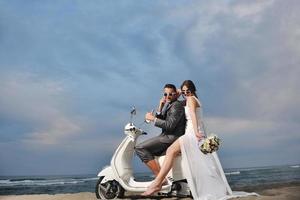 appena sposato coppia su il spiaggia cavalcata bianca scooter foto