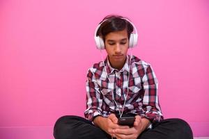 Arabo adolescenziale ragazzo indossare cuffie e ascoltando per musica rosa sfondo foto