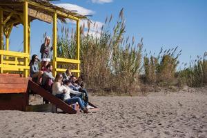 gruppo di amici avendo divertimento su autunno giorno a spiaggia foto