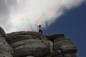 un' giovane ragazza a il picco di un' montagna e un' arcobaleno nel il cielo. foto