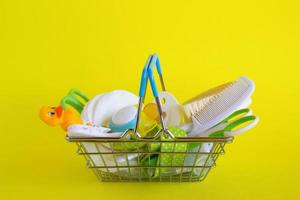 shopping cestino con bambino cura elementi - forbici, spazzole per capelli, ciucci, termometro, cotone pastiglie, pacificatore titolari e nasale aspiratore - su giallo sfondo. foto