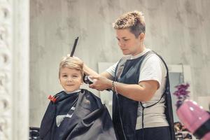 piccolo ragazzo ottenere un' taglio di capelli a barbiere negozio. foto