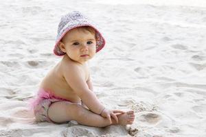 carino poco bambino ragazza nel rosa nuoto tronchi e Panama seduta su sabbia a spiaggia. foto