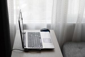 opera a partire dal casa su il tavolo con il computer portatile e grigio divano vicino per finestra. foto