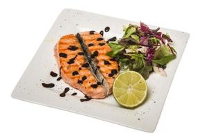 salato pesce porzione arrostito norvegese salmone filetto guarnito con insalata e basilico le foglie e lime su bianca piatto isolato con balsamico salse foto