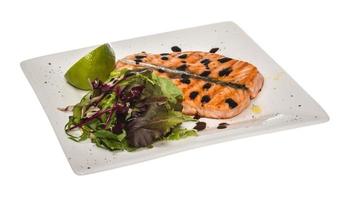 salato pesce porzione arrostito norvegese salmone filetto guarnito con insalata e basilico le foglie e lime su bianca piatto isolato con balsamico salse foto