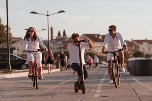 contento famiglia godendo un' bellissimo mattina di il mare insieme, genitori equitazione un' bicicletta e loro figlio equitazione un elettrico scooter. selettivo messa a fuoco foto