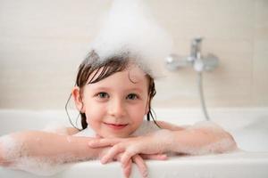 poco ragazza nel bagno giocando con schiuma foto