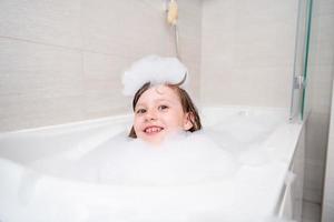 poco ragazza nel bagno giocando con schiuma foto