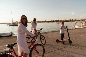 contento famiglia godendo un' bellissimo mattina di il mare insieme, genitori equitazione un' bicicletta e loro figlio equitazione un elettrico scooter. selettivo messa a fuoco foto