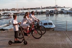 contento famiglia godendo un' bellissimo mattina di il mare insieme, genitori equitazione un' bicicletta e loro figlio equitazione un elettrico scooter. selettivo messa a fuoco foto