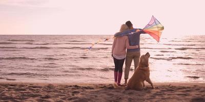 coppia con cane avendo divertimento su spiaggia su autunno giorno foto