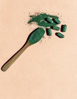 avvicinamento di clorella o spirulina compresse e un' di legno cucchiaio con polvere su un' leggero rosa sfondo nel il sole. nutritivo supplemento, disintossicazione superfood copia spazio foto