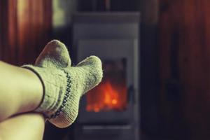 piedi gambe nel inverno Abiti lana calzini a camino sfondo. donna seduta a casa su inverno o autunno sera rilassante e riscaldamento su. inverno e freddo tempo metereologico concetto. hygge Natale vigilia. foto