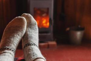 piedi gambe nel inverno Abiti lana calzini a camino sfondo. donna seduta a casa su inverno o autunno sera rilassante e riscaldamento su. inverno e freddo tempo metereologico concetto. hygge Natale vigilia. foto