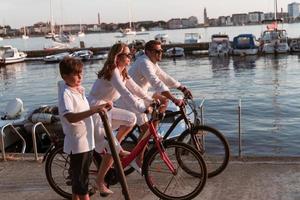 contento famiglia godendo un' bellissimo mattina di il mare insieme, genitori equitazione un' bicicletta e loro figlio equitazione un elettrico scooter. selettivo messa a fuoco foto