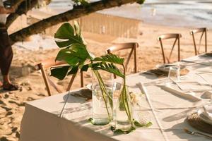 bellissimo tavolo impostato su per un' romantico cena su il spiaggia con fiori e candele. ristorazione per un' romantico Data, nozze o luna di miele sfondo. tramonto spiaggia cena. selezionato messa a fuoco. foto