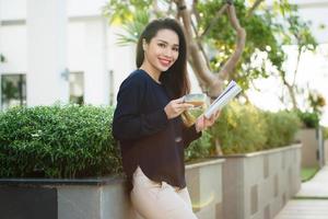 contento giovane donna Tenere libro affettuoso di letteratura analizzando romanzo durante tempo libero tempo su terrazza di città universitaria bar nel soleggiato giorno. foto