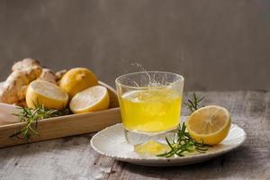 Zenzero tè con Limone, Zenzero radice e rosmarino su di legno sfondo. piccolo bicchiere trasparente brocca con caldo bere. di stagione bevande. superficiale dof, selettivo messa a fuoco, messa a fuoco su superiore di brocca. foto