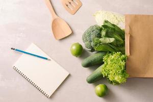 carta Borsa pieno di salutare cibo con taccuini su un' grigio sfondo. superiore Visualizza. piatto posare foto