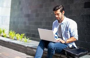 giovane caucasico uomo seduta e Lavorando su libero professionista progetto utilizzando portatile computer a esterno ufficio. foto