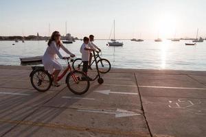 contento famiglia godendo un' bellissimo mattina di il mare insieme, genitori equitazione un' bicicletta e loro figlio equitazione un elettrico scooter. selettivo messa a fuoco foto