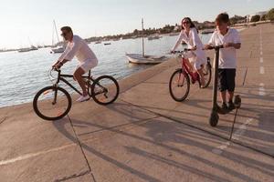 contento famiglia godendo un' bellissimo mattina di il mare insieme, genitori equitazione un' bicicletta e loro figlio equitazione un elettrico scooter. selettivo messa a fuoco foto