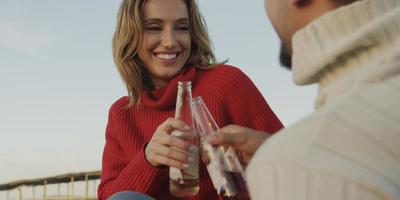 amorevole giovane coppia seduta su il spiaggia accanto fuoco di bivacco potabile birra foto