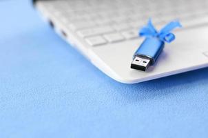 brillante blu USB veloce memoria carta con un' blu arco bugie su un' coperta di morbido e peloso leggero blu vello tessuto accanto per un' bianca il computer portatile. classico femmina regalo design per un' memoria carta foto