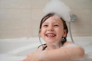 poco ragazza nel bagno giocando con schiuma foto