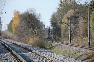 autunno industriale paesaggio. ferrovia sfuggente in il distanza tra verde e giallo autunno alberi foto