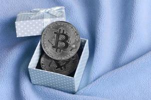 il argento bitcoin bugie nel un' piccolo blu regalo scatola con un' piccolo arco su un' coperta fatto di morbido e soffice leggero blu vello tessuto con un' grande numero di sollievo pieghe foto