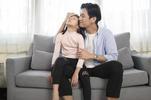 ritratto di asiatico padre e figlia seduta su divano nel il vivente camera foto