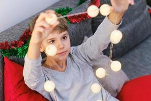 ritratto di un' Natale ragazzo. il bambino prepara Natale luci per decorare il Casa. foto