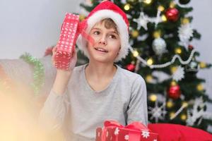 un' contento bambino nel un' Santa Claus cappello si apre Natale i regali. foto