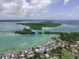 aereo Visualizza di villaggio vicino bellissimo spiaggia con piccolo isola nel il sfondo nel maluku, Indonesia foto