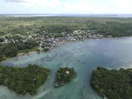 aereo Visualizza di villaggio vicino bellissimo spiaggia con piccolo isola nel il sfondo nel maluku, Indonesia foto