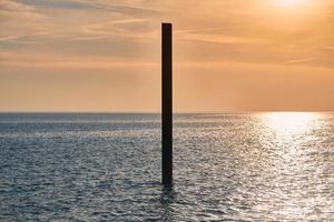 grande pilastro di costruzione in acciaio arrugginito nel mare blu con onde calme al tramonto, parte di edificio abbandonata foto