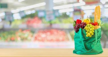 frutta e verdura fresca in una borsa della spesa verde riutilizzabile sul tavolo di legno con supermercato negozio di alimentari sfocato sfondo sfocato con luce bokeh foto