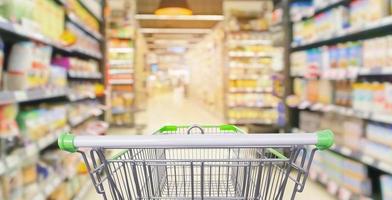 carrello della spesa nel corridoio del supermercato con gli scaffali dei prodotti interni sfocati sfocatura dello sfondo foto