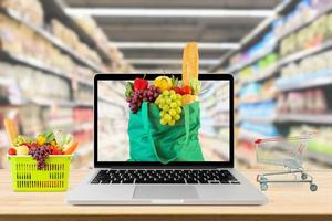 supermercato corridoio sfocato sfondo con il computer portatile computer e shopping carrello su legna tavolo drogheria in linea concetto foto