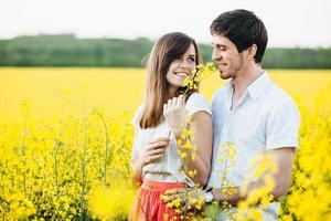 scatto all'aperto di una coppia adorabile in piedi l'uno vicino all'altro, abbracciarsi e guardarsi negli occhi, posare su uno sfondo di campo giallo, godersi un'atmosfera calma e armonia con la natura. concetto di amore e persone foto