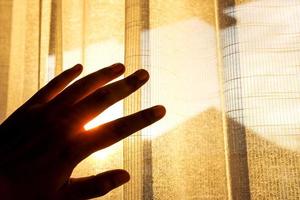 pelle o occhi protezione concetto. mano sollevato su per proteggere un' estate luce del sole dentro un' Casa. tenda vedere attraverso e sunburst come sfondo foto